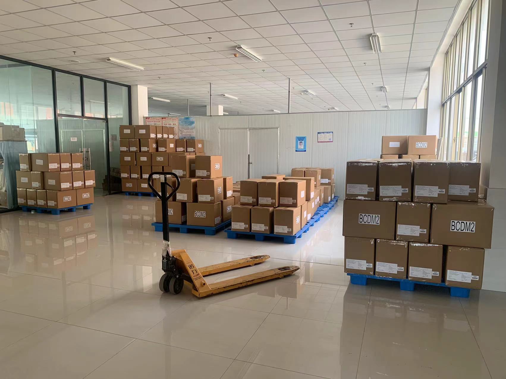 Finished goods storage & operation area in garment factory with carton goods, manual hydraulic truck & pallets, suitable for finished goods storage and logistics handling preparation.
