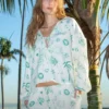 100% linen printed loungewear set with green palm tree and circle prints on white background, including a tie - front top and matching pants, casual and vacation - ready design against palm tree backdrop