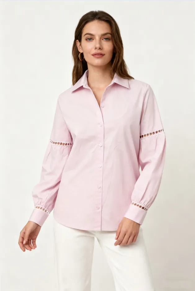Woman wearing a light pink collared shirt with lace - cutout details on sleeves and white pants