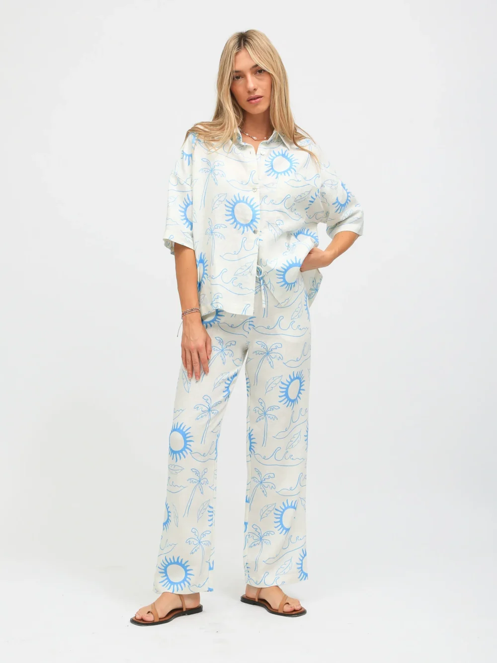 100% linen printed summer loungewear set with blue sun and palm tree prints on white background, shirt and wide - leg pants design