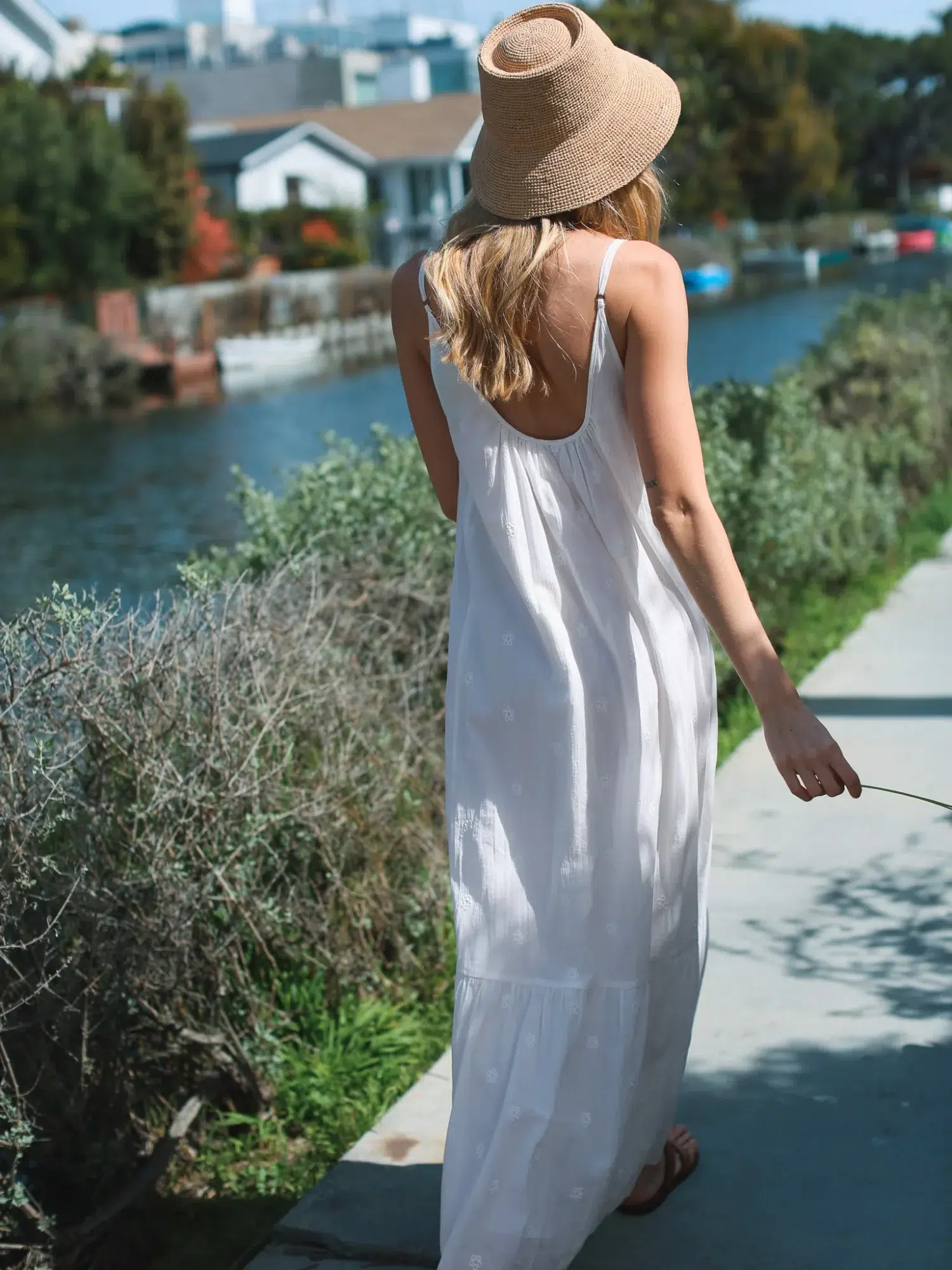 100% cotton embroidered spaghetti - strap maxi dress in white with embroidery details, styled with straw hat in outdoor casual scene
