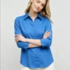 Woman wearing a bright blue collared shirt with 3/4 sleeves and white pants
