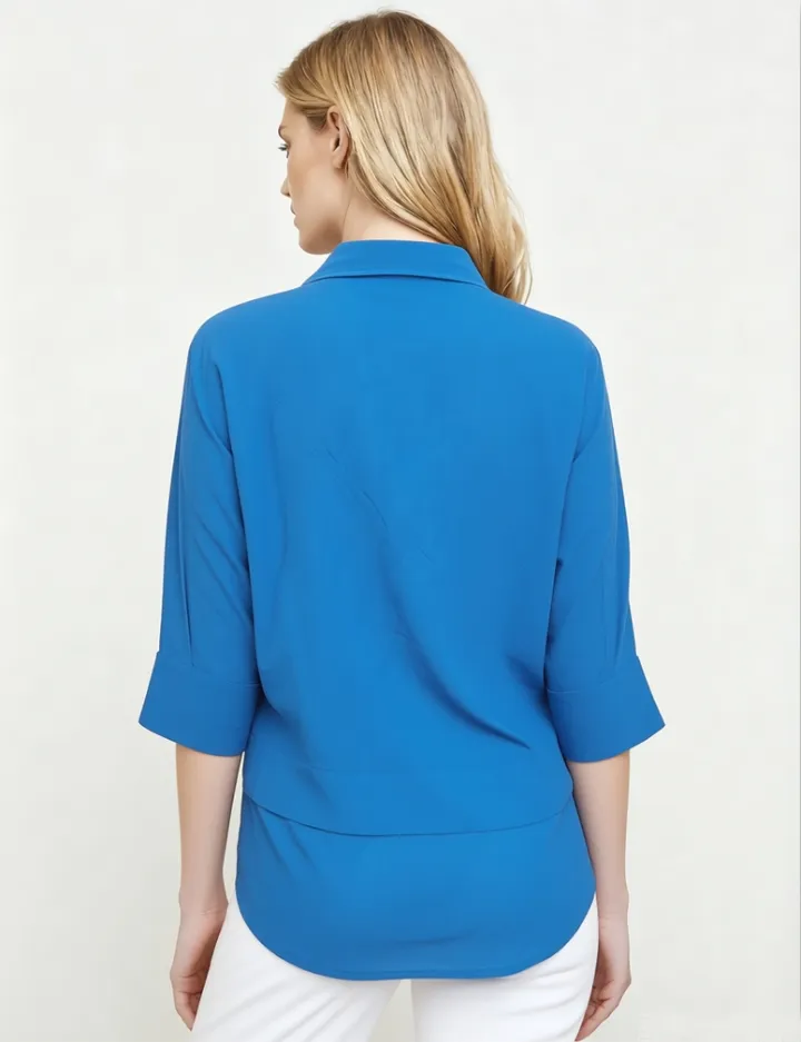 Back view of a woman wearing a bright blue collared shirt with 3/4 sleeves and white pants