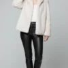 light beige faux fur short Smoothie Jacket- front view Woman wearing a light beige faux fur short coat, white top, black leather pants, and black knee - high boots against a light gray background.