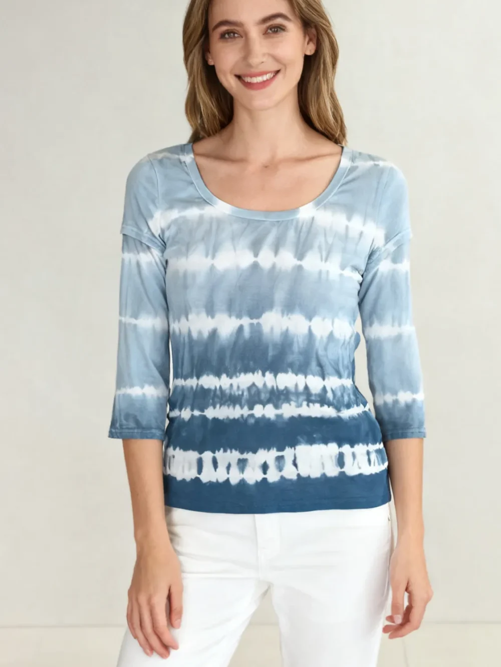 Woman wearing a blue and white tie - dye three - quarter sleeve top with white pants against a light background.