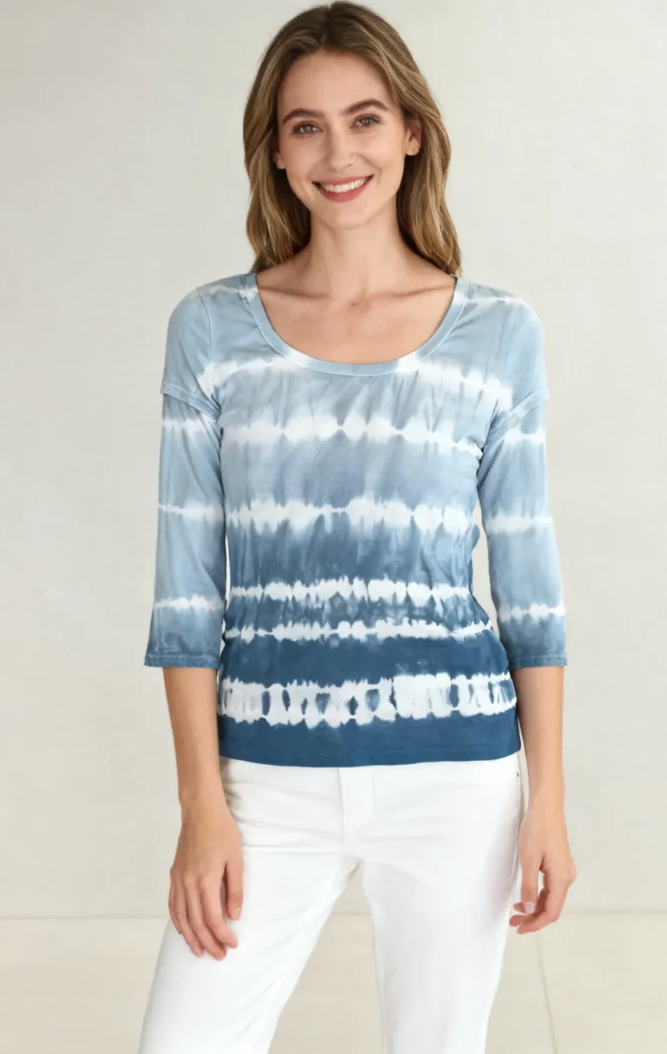 Woman wearing a blue and white tie - dye three - quarter sleeve top with white pants against a light background.