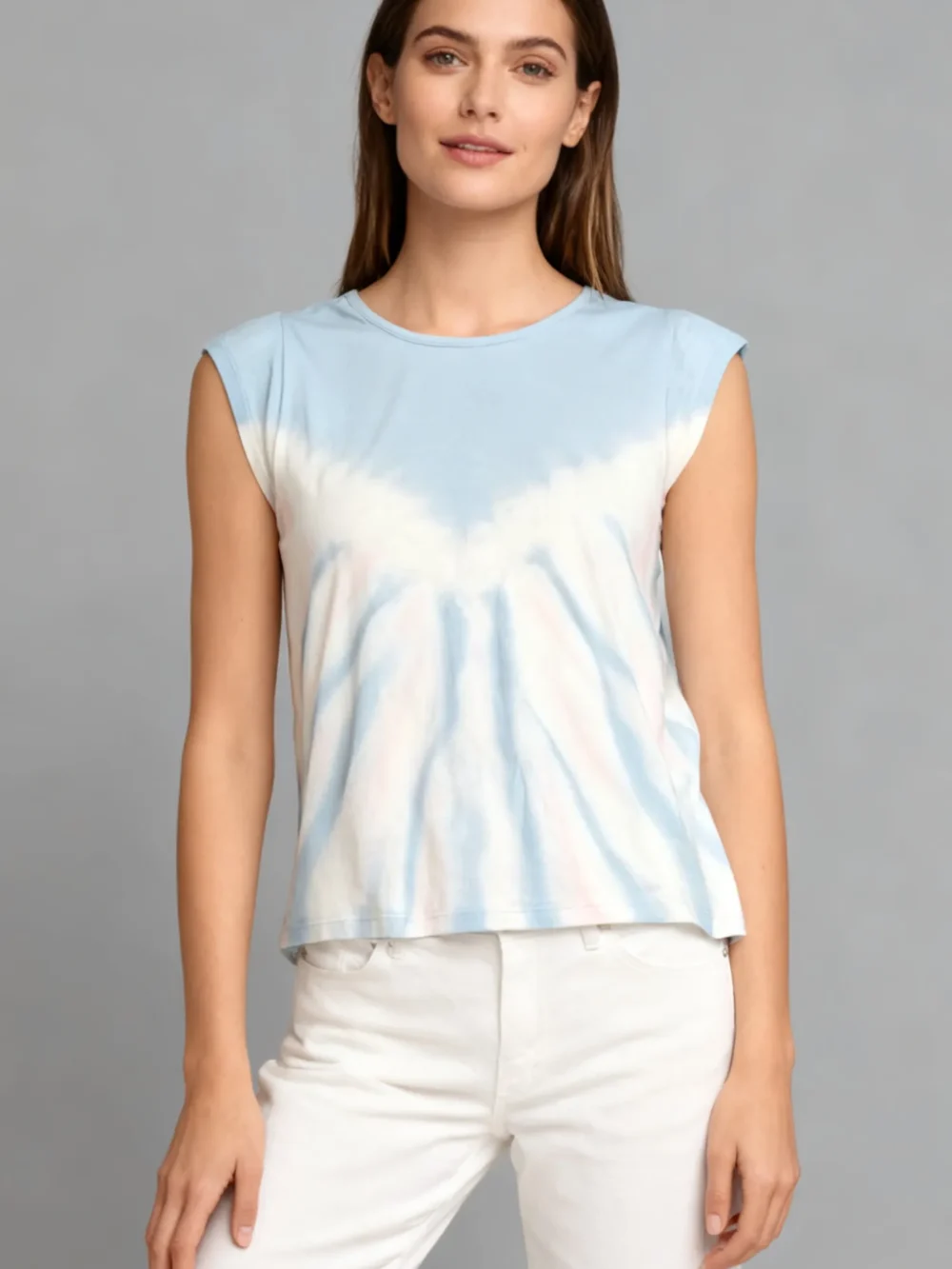 Woman wearing a blue and white tie - dye sleeveless top with white pants against a light gray background.