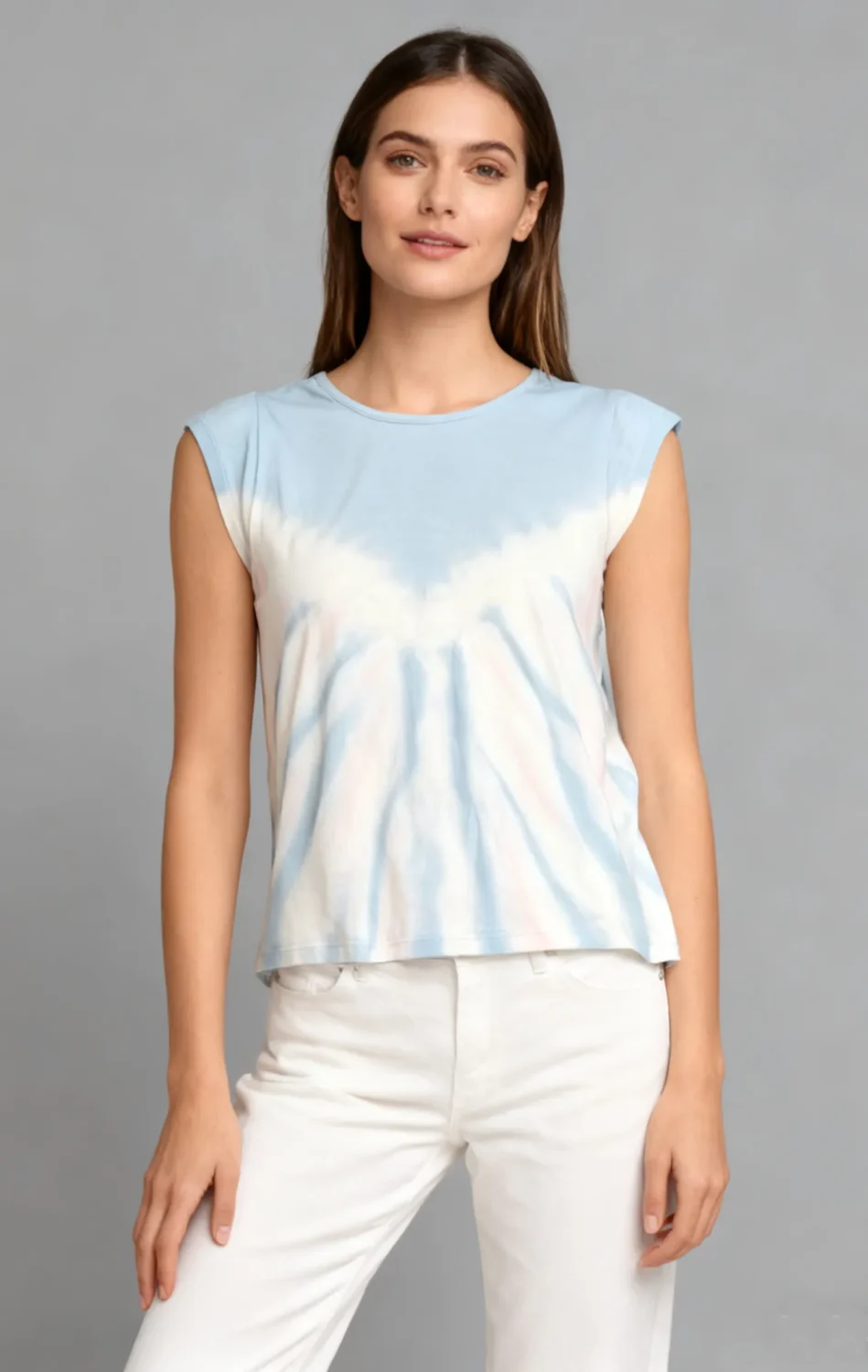 Woman wearing a blue and white tie - dye sleeveless top with white pants against a light gray background.