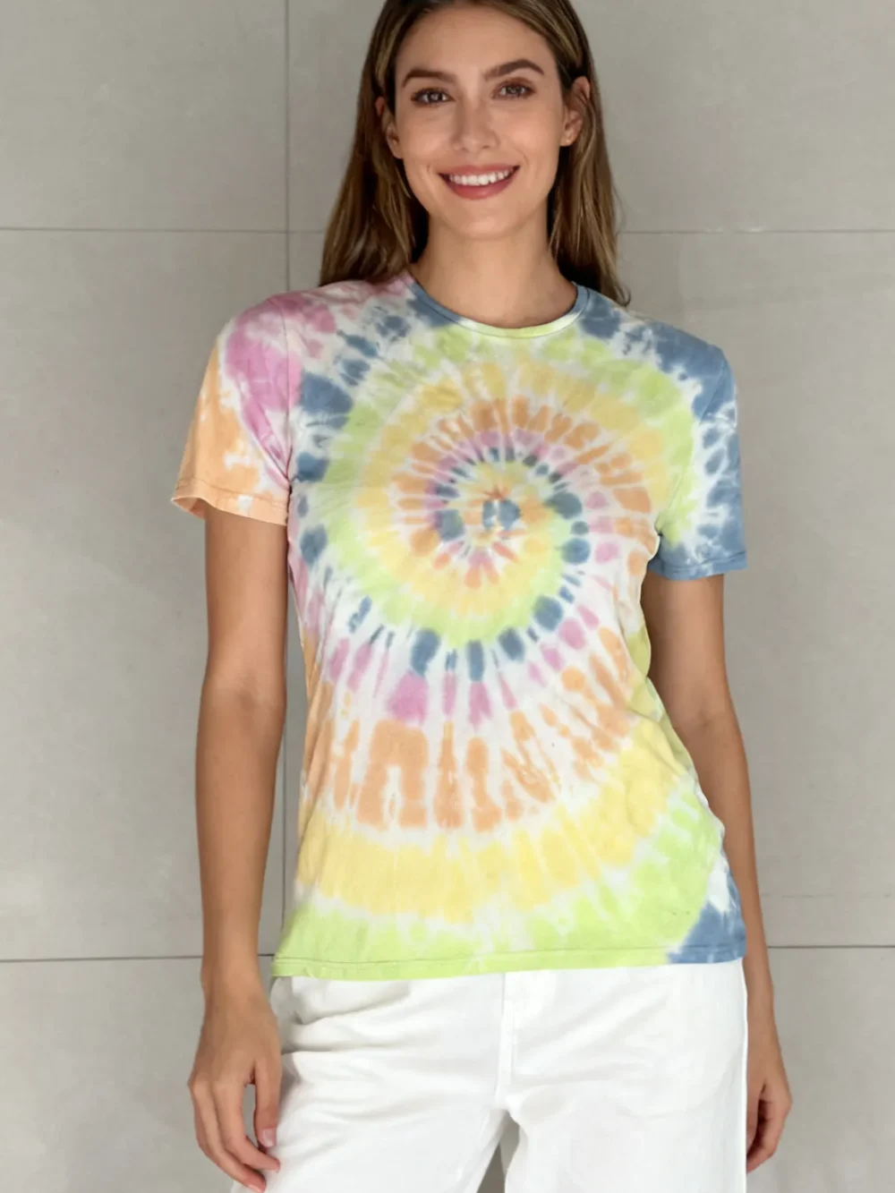Woman wearing a rainbow spiral tie - dye short sleeve t - shirt with white pants against a light