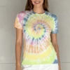 Woman wearing a rainbow spiral tie - dye short sleeve t - shirt with white pants against a light