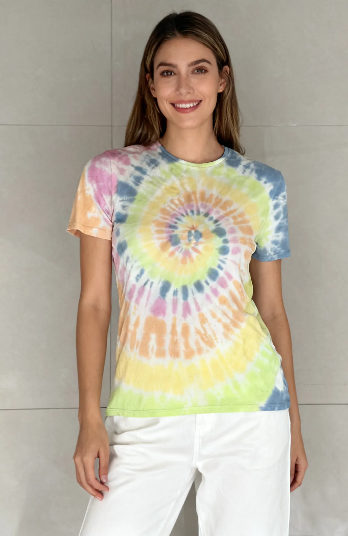 Woman wearing a rainbow spiral tie - dye short sleeve t - shirt with white pants against a light