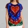 Woman wearing a multicolor heart tie - dye short sleeve top with white pants against a light gray background.