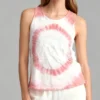 Woman wearing a pink and white spiral tie - dye sleeveless tank top with white pants against a light gray