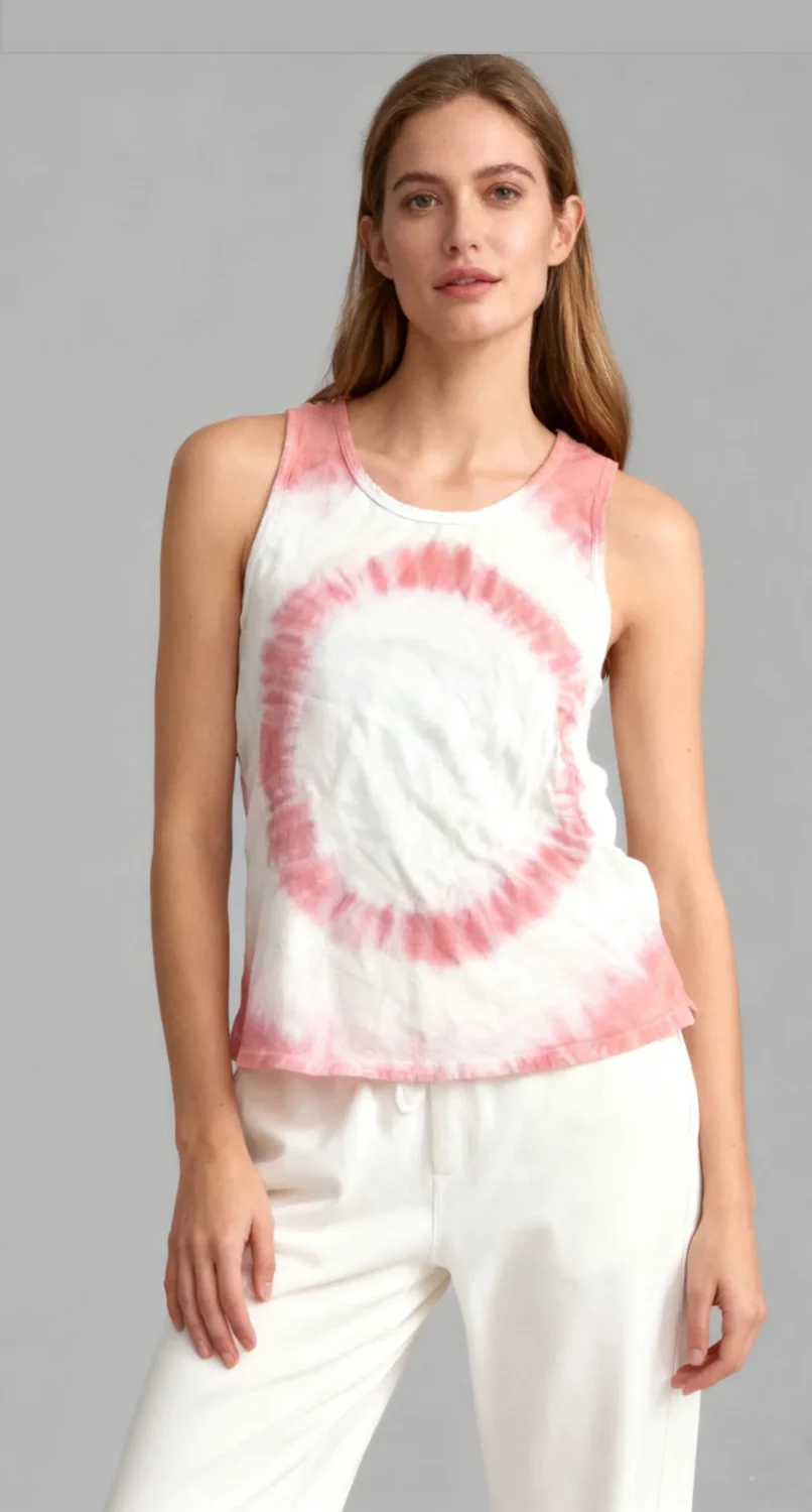 Woman wearing a pink and white spiral tie - dye sleeveless tank top with white pants against a light gray
