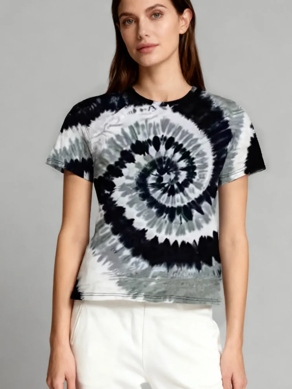 Woman wearing a black and white spiral tie - dye short sleeve t - shirt with white pants against a light gray background.