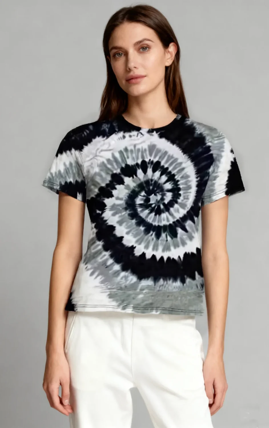 Woman wearing a black and white spiral tie - dye short sleeve t - shirt with white pants against a light gray background.