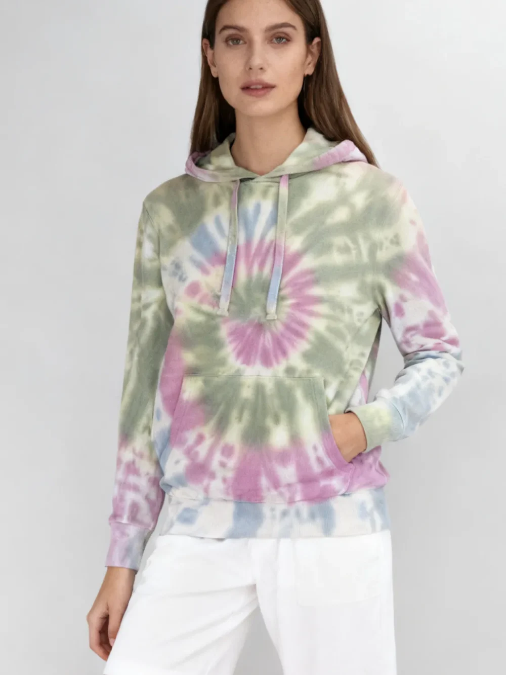 Woman wearing a pastel spiral tie - dye hoodie with white shorts against a light gray background.