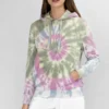 Woman wearing a pastel spiral tie - dye hoodie with white shorts against a light gray background.
