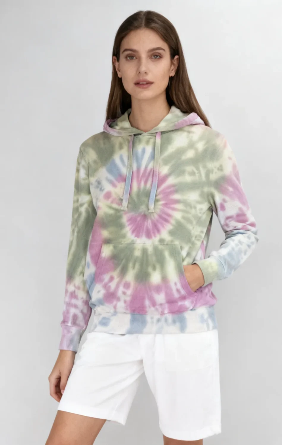 Woman wearing a pastel spiral tie - dye hoodie with white shorts against a light gray background.