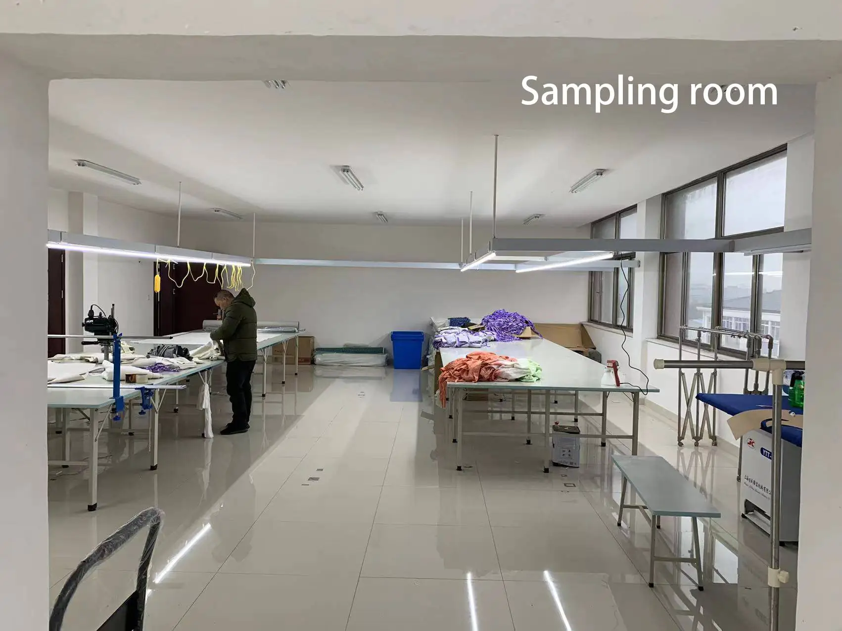Garment sampling room with operating tables, various fabrics & semi-finished products, suitable for sample development & sorting.
