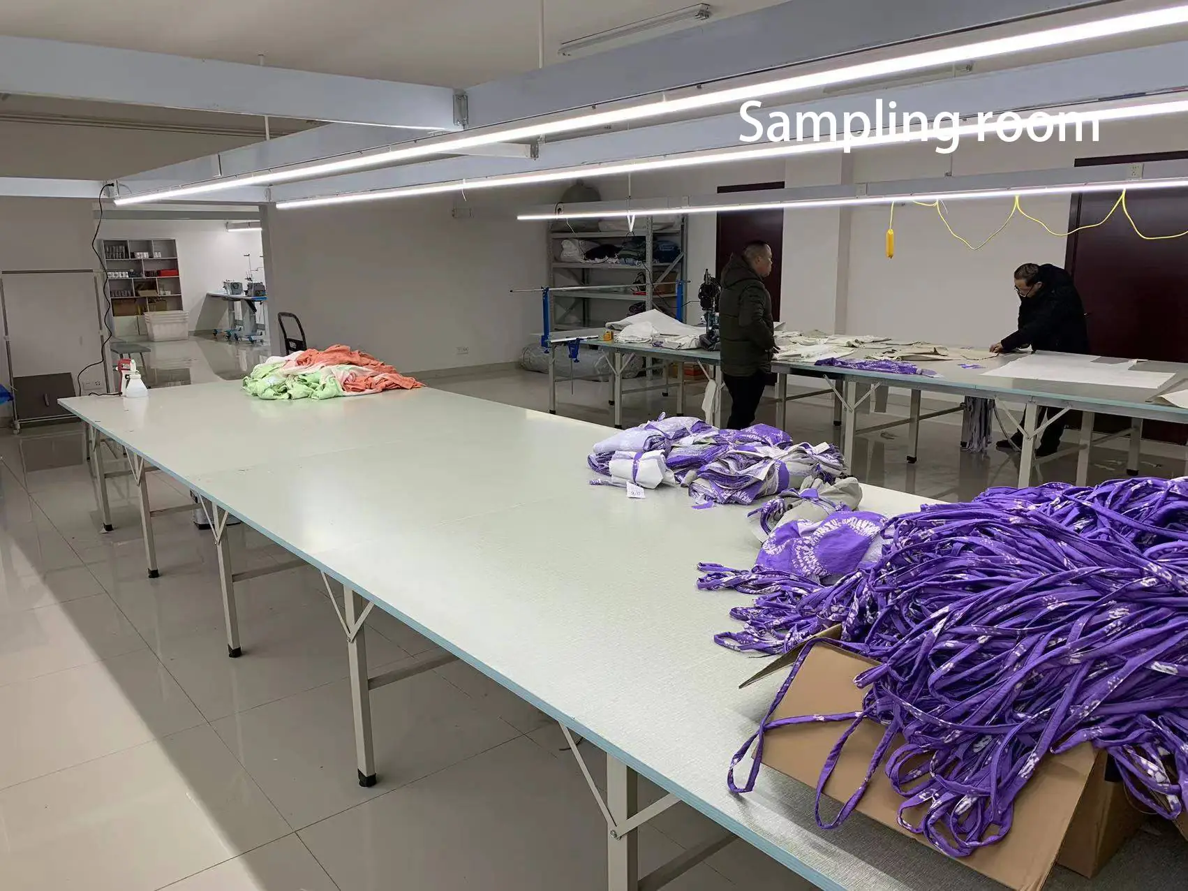 Garment sampling room with operating tables, various fabrics & semi-finished products, suitable for sample development & sorting.