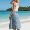 Embroidered patchwork denim midi skirt paired with a white tank top, featuring a casual style, suitable for vacation or beach-side daily wear (with a beach, blue sea, and island background).