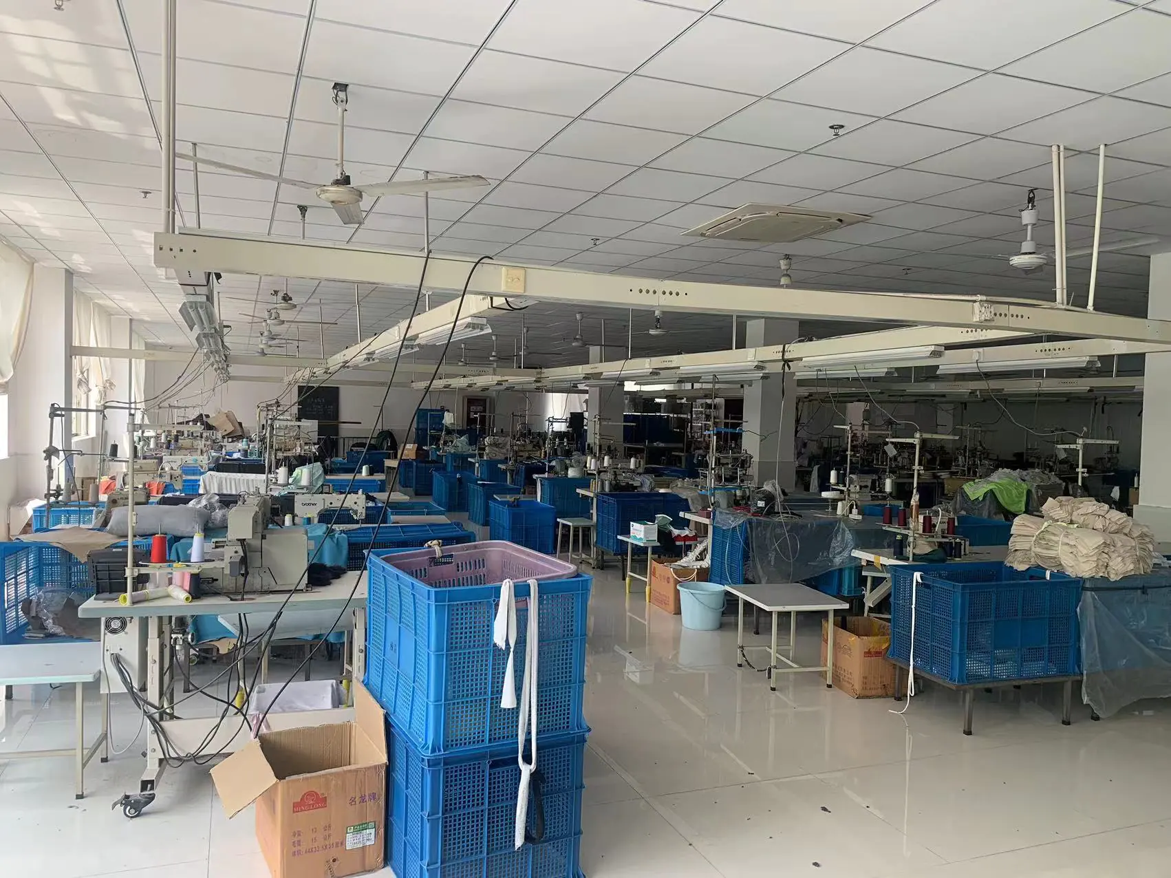 Sewing workshop in garment factory with sewing machines & blue turnover baskets, orderly for garment sewing production.