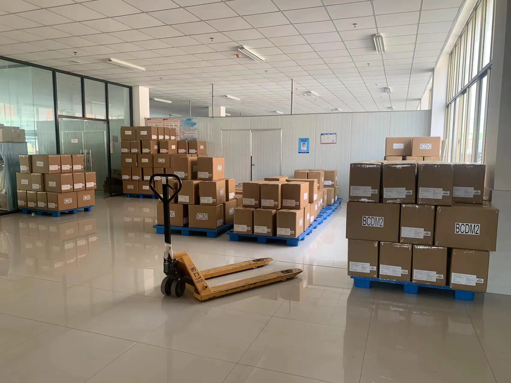 Finished goods storage & operation area in garment factory with carton goods, manual hydraulic truck & pallets, suitable for finished goods storage and logistics handling preparation.