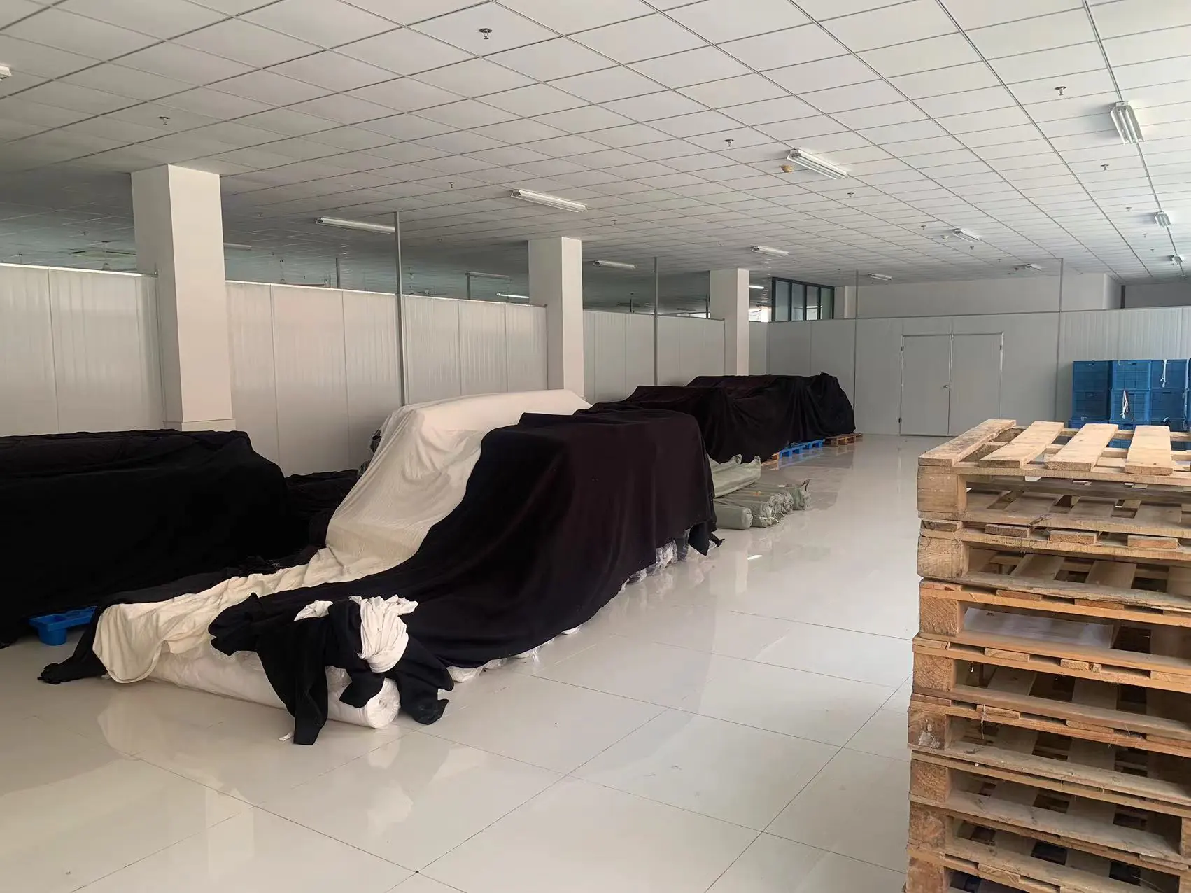 Fabric warehouse in garment factory with covered fabric goods & pallets, tidy & orderly for fabric storage.