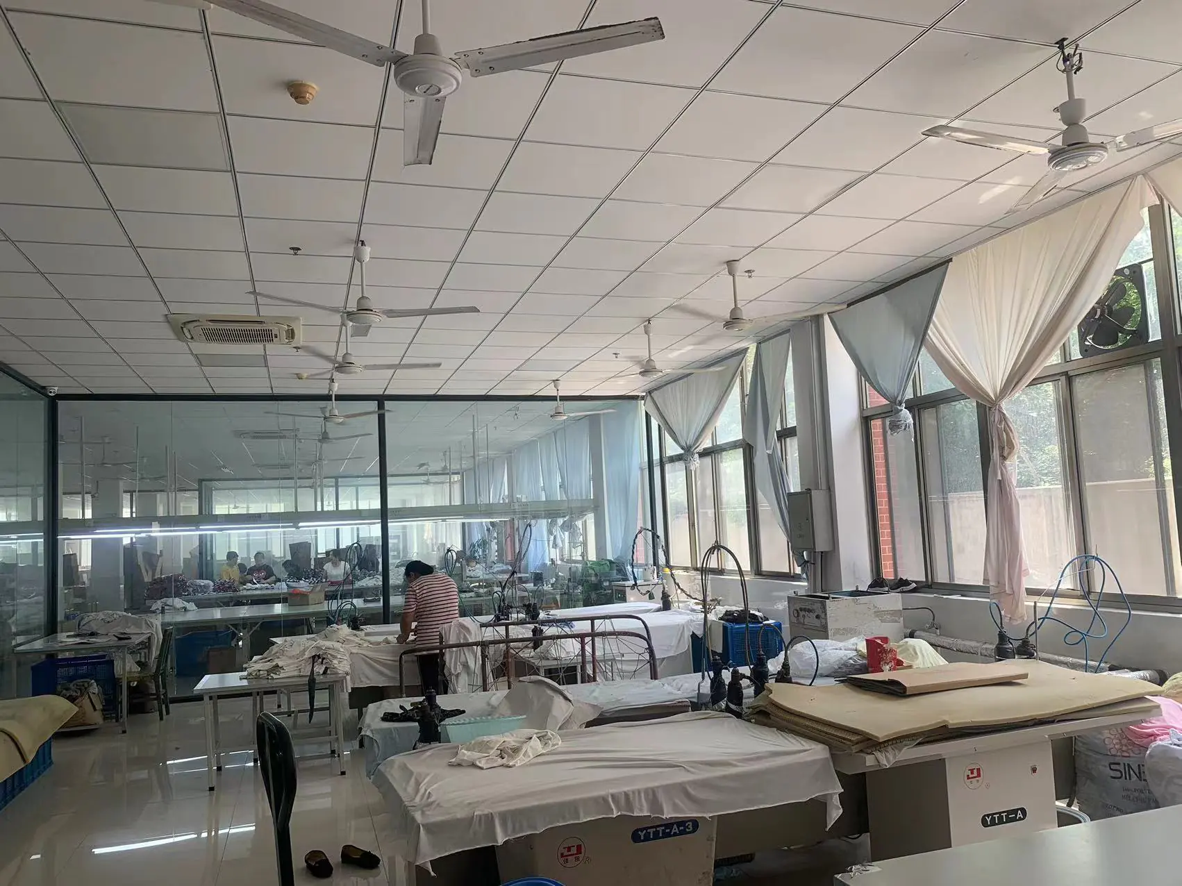 Clothing production workshop interior with machinery, fabrics, and workers, showing garment manufacturing environment.