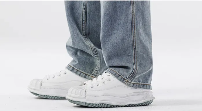 Detail view of light blue loose-fit jeans’ hem and matching white shoes