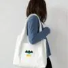 Model carrying white canvas tote bag with "3Nice" text and landscape graphic