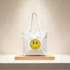 smiley-face-canvas-tote-bag-still-life.jpg White canvas tote bag with yellow smiley face (still life)
